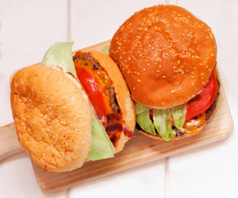 Metro Canteens Adelaide, Canteen Suppliers in Adelaide image of two hamburgers on a wooden chopping board.