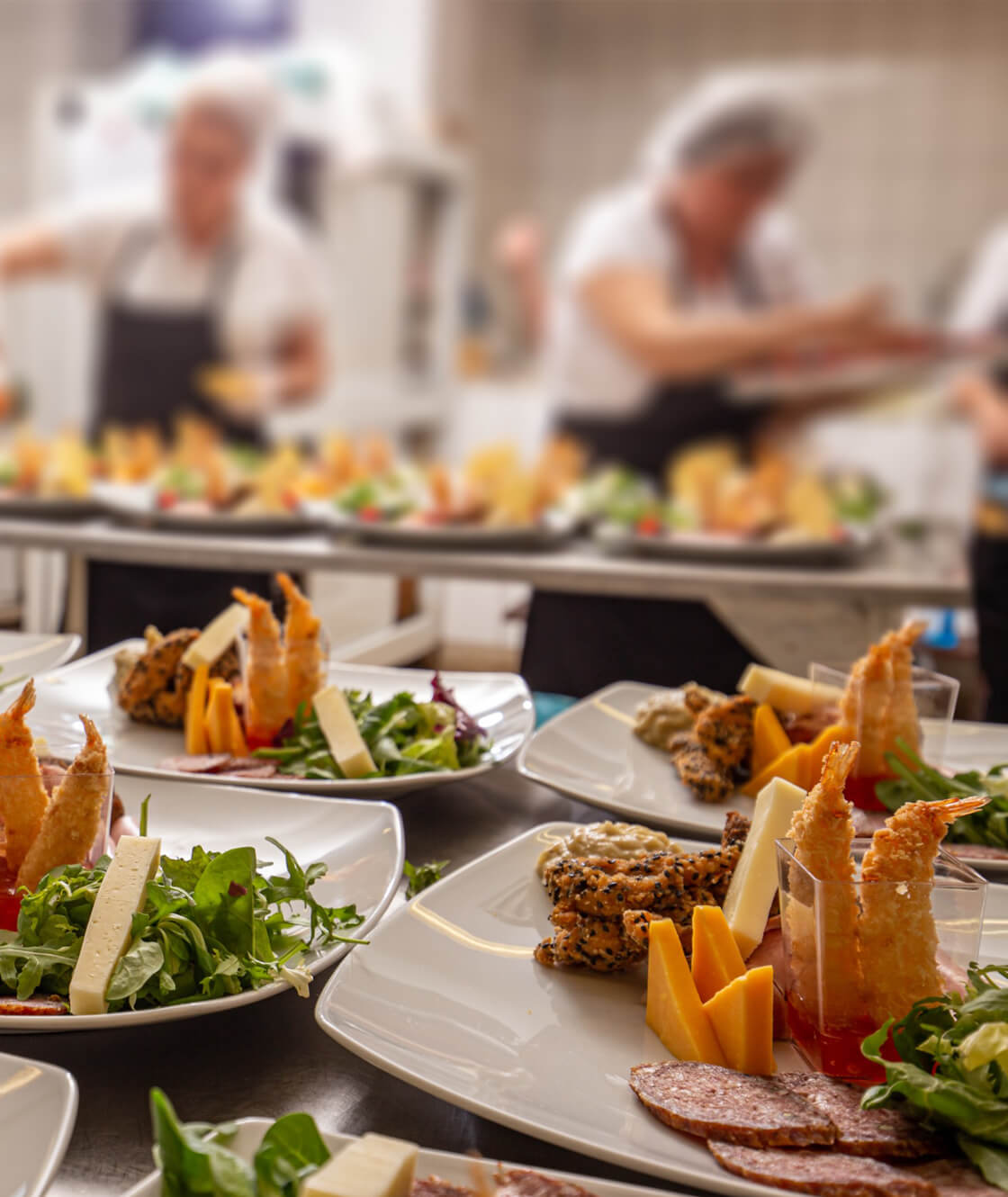 Metro Canteens catering Adelaide, image of caterers preparing plates of food. Completed plates of food in the foreground.