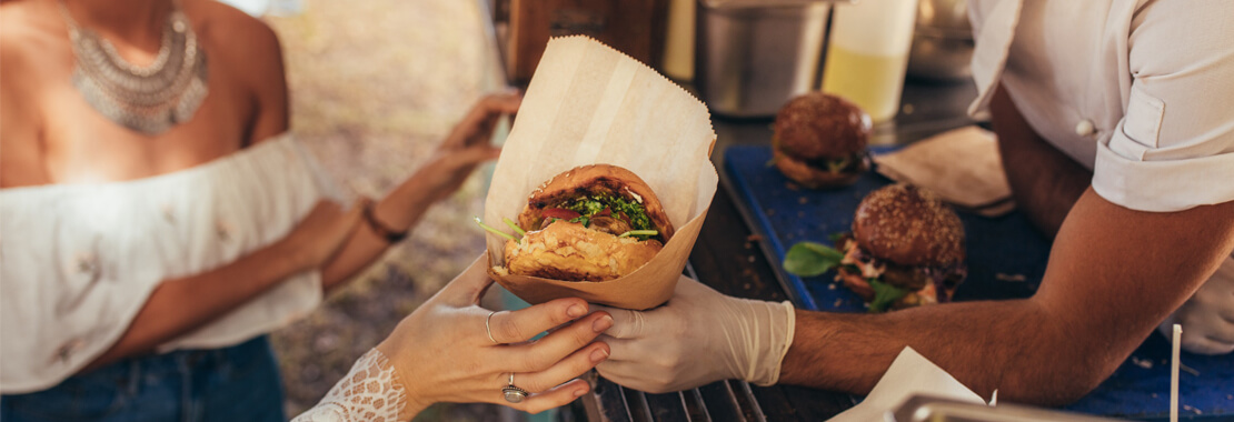 Metro Canteens Adelaide - Mobile Food Truck page image of a food truck cook handing a delicious hamburger to a customer.