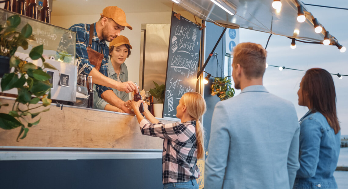 Metro Canteens Adelaide - Mobile Food Truck page image of a young lady purchasing food and drink at a fook truck with a young couple cued behind her.